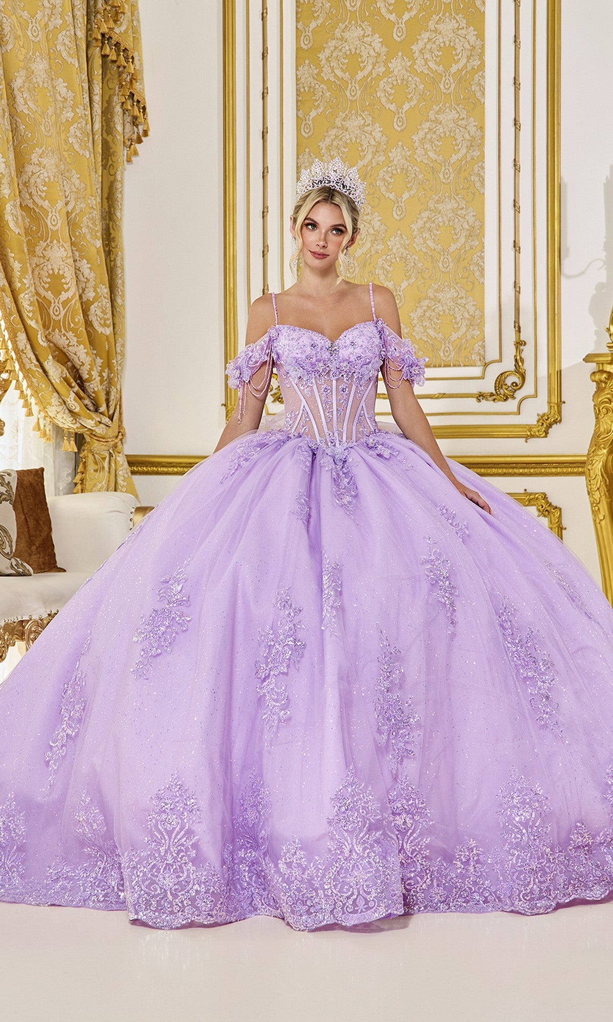 A woman in the Quinceanera Dress 5093 by Dancing Queen, in lilac with floral embroidery and a tiara, stands in an ornate room with gold and white decor.